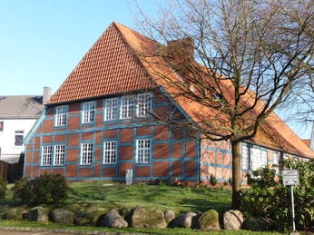 Clüverhaus Rückansicht Backstein-Fachwerkhaus mit rotem Satteldach, umgeben von grüner Wiese und Steinweg im Vordergrund.