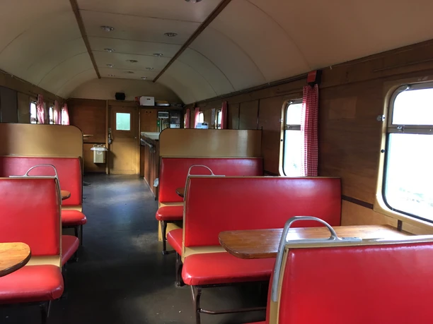 historischer Waggon Innenansicht eines nostalgischen Eisenbahnwaggons mit roten Sitzen und Holztischen.