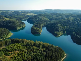 Genkeltalsperre <p>Luftaufnahme eines üppigen, grünen Waldes durchzogen von einem ruhigen, blauen Fluss, sanfte Hügel im Hintergrund.</p>