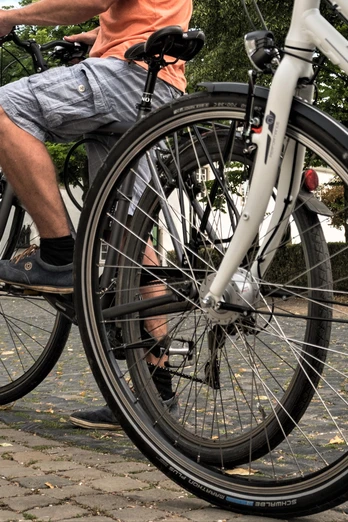 Zwei Personen auf Fahrrädern fahren auf einem gepflasterten Weg vor einem historischen Gebäude.