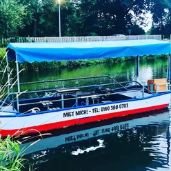 Harener Bootsverleih Motorboot mit blauem Sonnendach liegt an einem grünen Ufer im ruhigen Wasser von Haren.