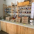 Meyers Hofladen2.jpg In einem gemütlichen Laden sind Holzbretterregale mit frischen Eiern und hausgemachten Marmeladen gefüllt.