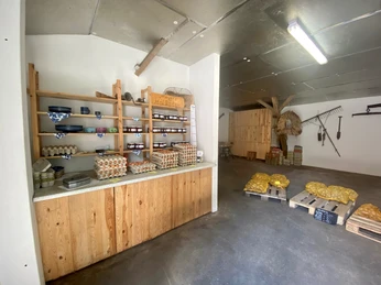 Meyers Hofladen1.jpg Innenansicht von Meyers Hofladen mit Holzregalen, die verschiedene lokale Produkte wie Eier, Brot und eingemachte Waren präsentieren.