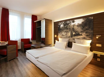 Gieschens Hotel Modern eingerichtetes Hotelzimmer mit Holzmöbeln, zwei Betten, roter Dekoration und Elefantenbild.