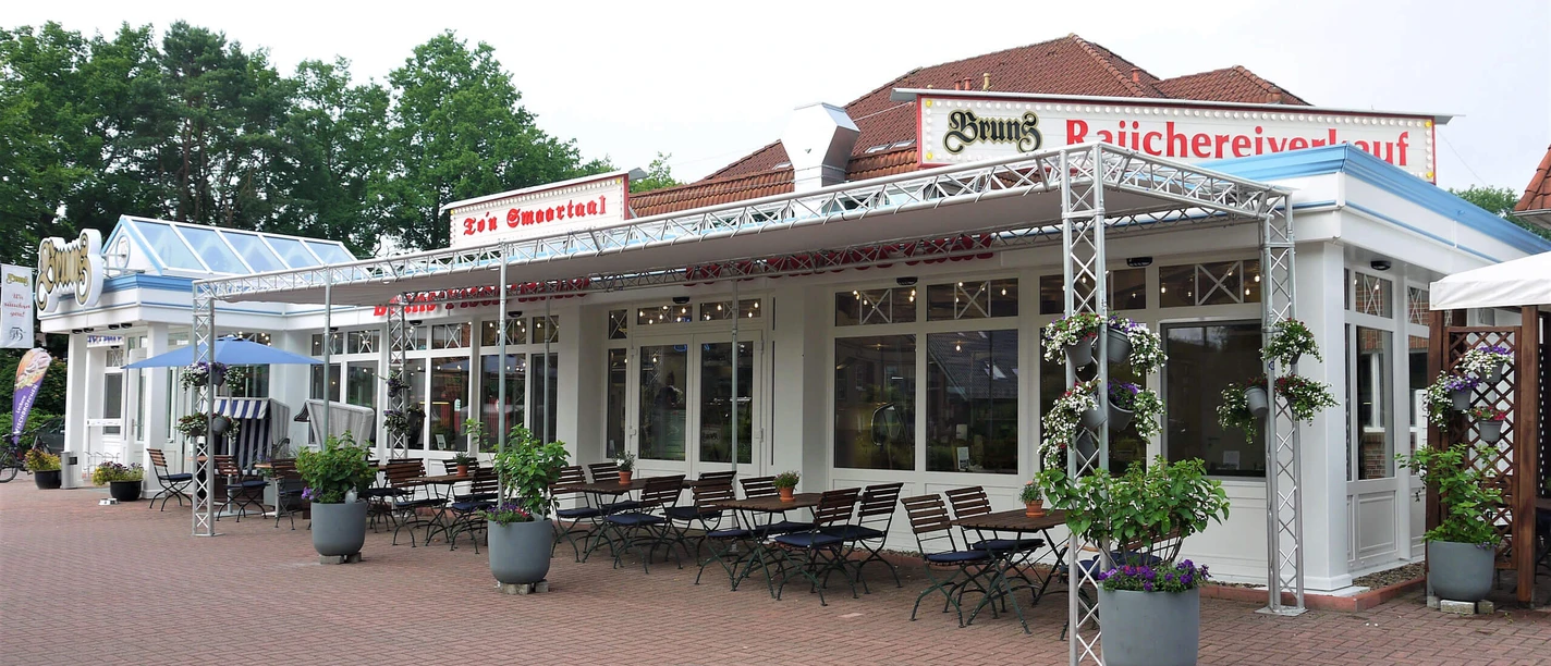 smoortaal-aussenansicht.jpg Das Bild zeigt die Außenterrasse eines Restaurants mit Sitzgelegenheiten und Blumenarrangements.