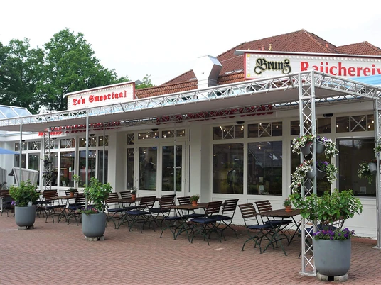 smoortaal-aussenansicht.jpg Das Bild zeigt die Außenterrasse eines Restaurants mit Sitzgelegenheiten und Blumenarrangements.