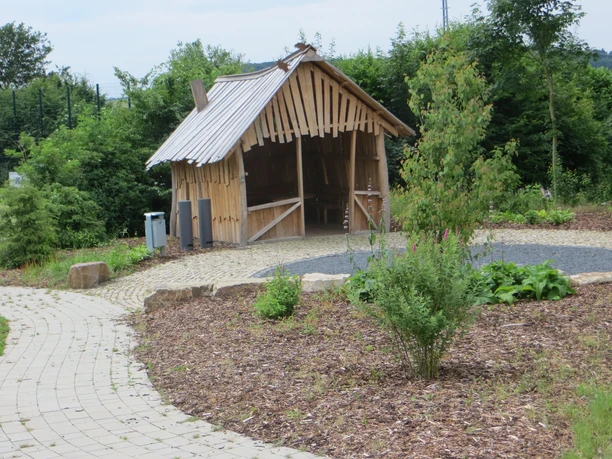 Kleiner hölzerner Pavillon in einem gepflegten Garten mit gepflasterten Wegen und grünen Büschen.
