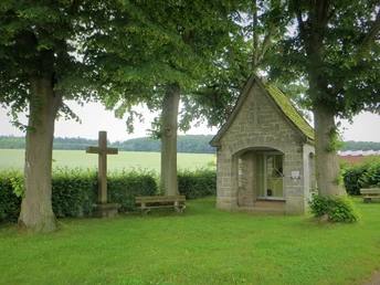 Marienkapelle bei Bökendorf Steinerne Marienkapelle bei Bökendorf, umgeben von Bäumen, mit Kreuz und Bänken, Felder im Hintergrund.
