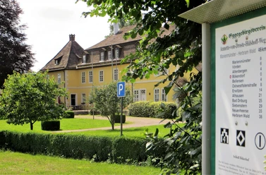 Schloss Bökerhof Gelbes Herrenhaus mit schiefergedecktem Dach und zahlreichen Fenstern, umgeben von gepflegtem Grün.