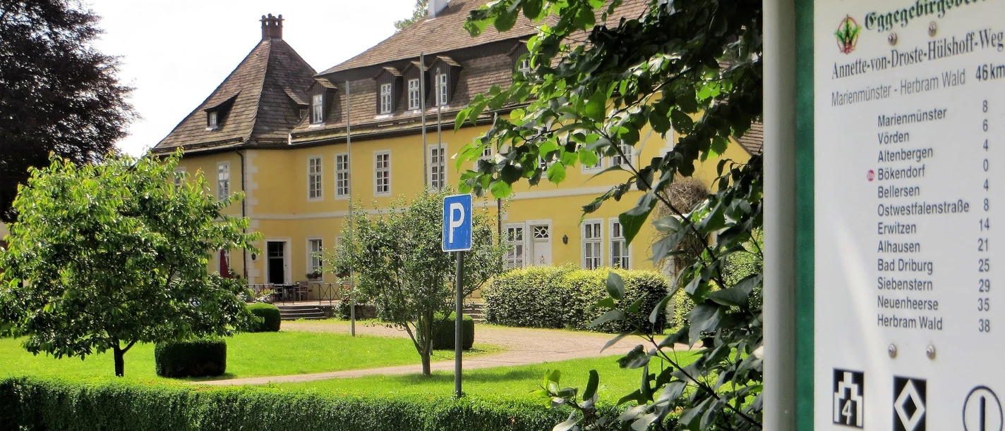 Schloss Bökerhof Gelbes Herrenhaus mit schiefergedecktem Dach und zahlreichen Fenstern, umgeben von gepflegtem Grün.