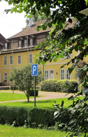 Schloss Bökerhof Gelbes Herrenhaus mit schiefergedecktem Dach und zahlreichen Fenstern, umgeben von gepflegtem Grün.