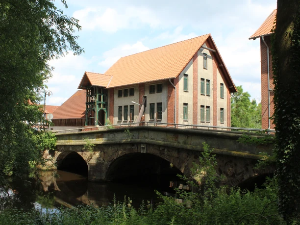 Historische Wassermühle in Steyerberg, eingebettet neben einer Brücke, mit markantem Fachwerkstil.