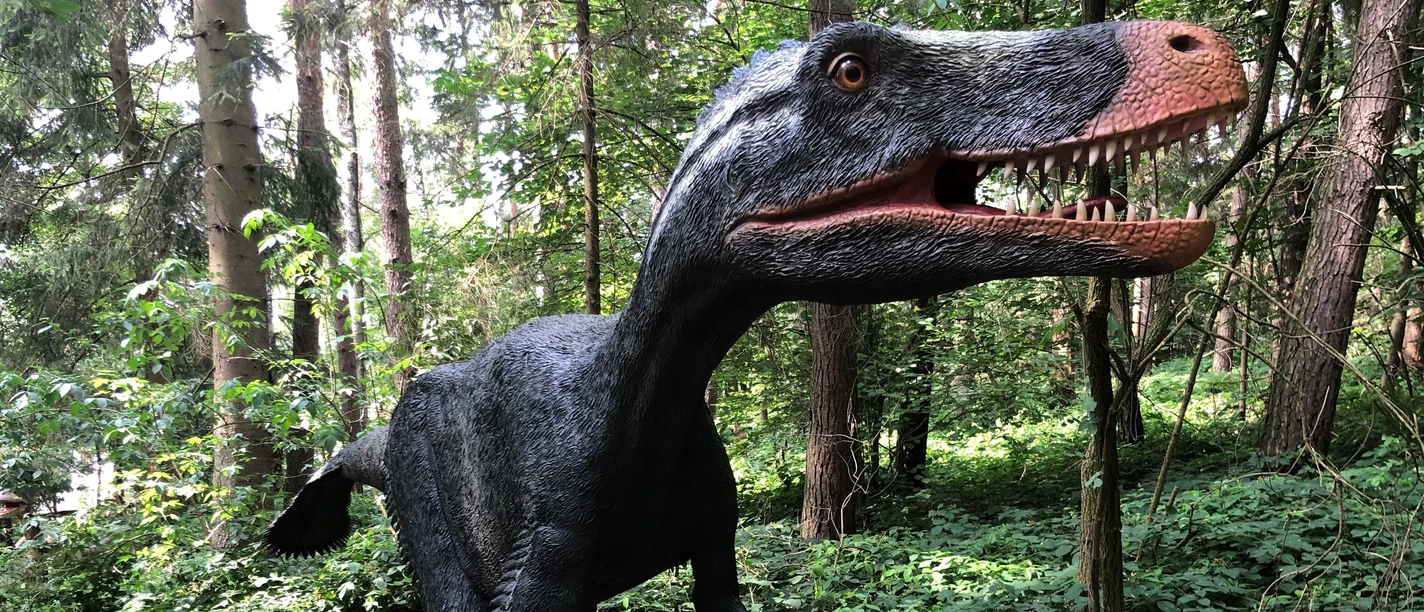 Dino-Park Ein lebensgroßer Dinosaurier steht im dichten Wald, zeigt Zähne und bewegt sich durch das grüne Dickicht.