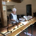 Stutenverkauf Eine ältere Frau verkauft frisch gebackenen Stuten an einem langen Holztisch.