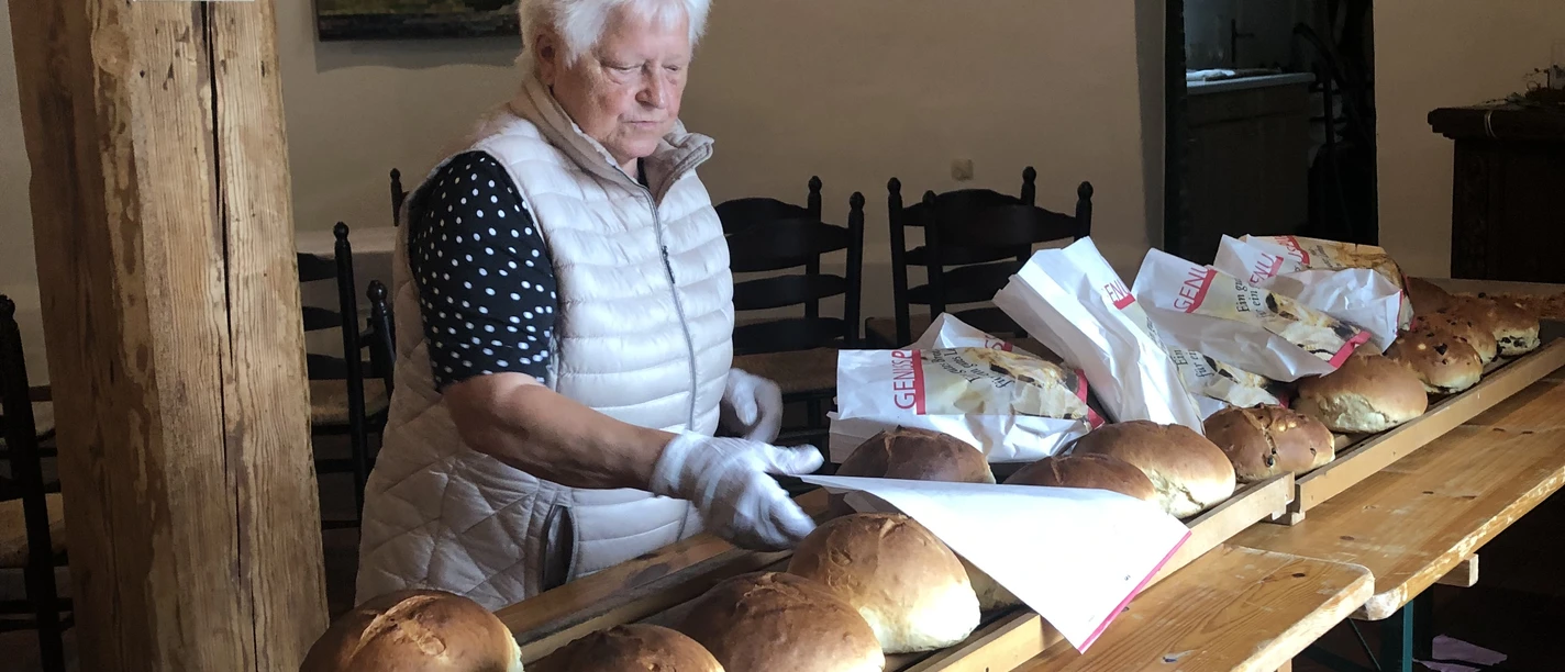 Stutenverkauf Eine ältere Frau verkauft frisch gebackenen Stuten an einem langen Holztisch.