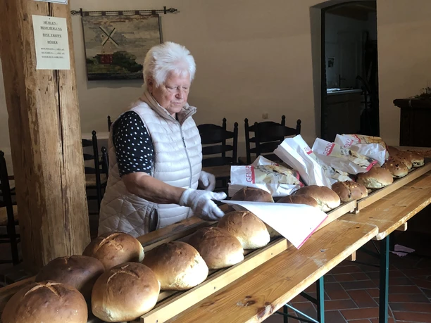 Stutenverkauf Eine ältere Frau verkauft frisch gebackenen Stuten an einem langen Holztisch.