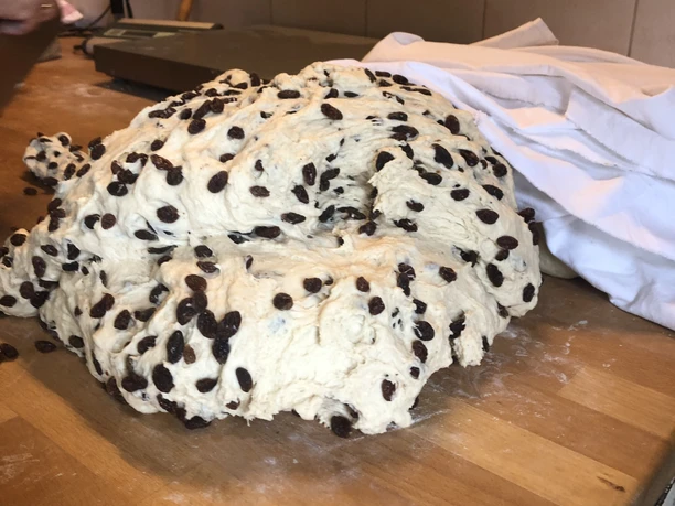 Rosinenstutenteig Ein massiver Rosinenstutenteig liegt auf einem Holztisch, besprenkelt mit zahlreichen Rosinen.