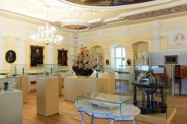 Interior of a museum with historical ship models and paintings under an ornate ceiling.
