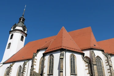Torgau-Marienkirche_WG_DSCF6629.jpg Weiße Kirche mit roten Ziegeldächern und gotischen Fenstern unter strahlend blauem Himmel.