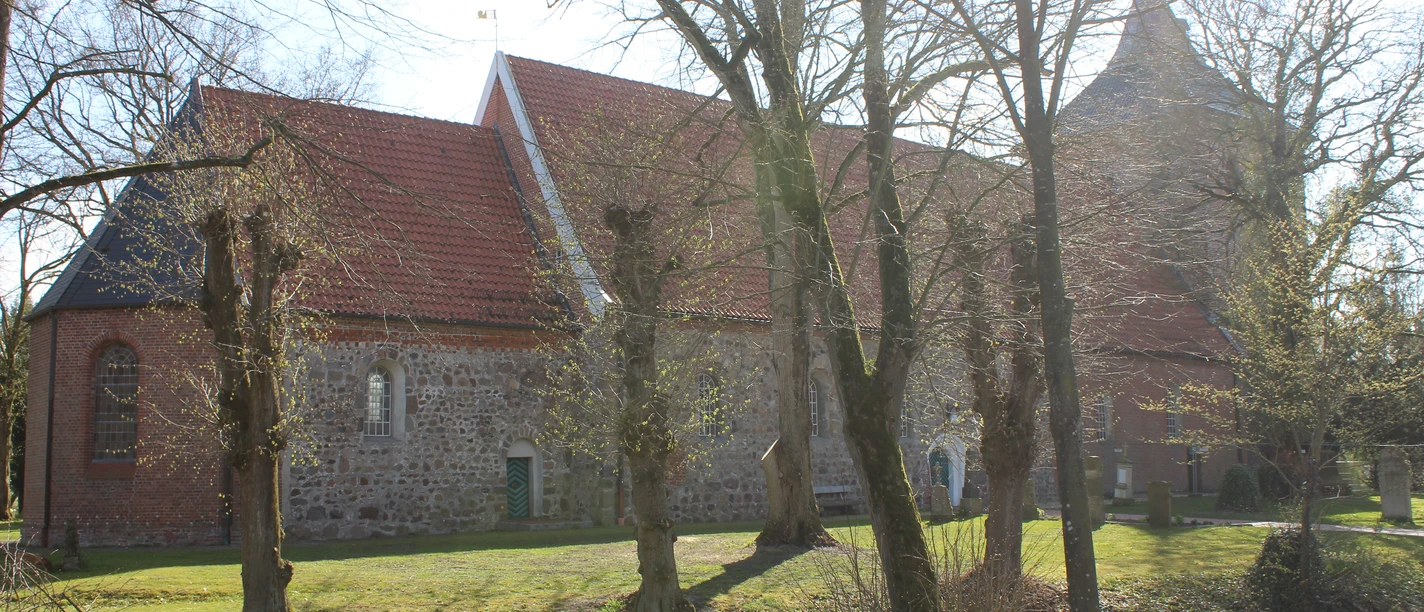 The historic St. Nicolai Church in Nordleda, with its fieldstone walls and expansive lawn bathed in sunlight.
