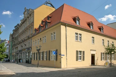 008 - Robert Schumann Haus - © Kultour Z.jpg Das Robert Schumann Haus in Zwickau mit gelber Fassade und rotem Dach an einer gepflasterten Straße.