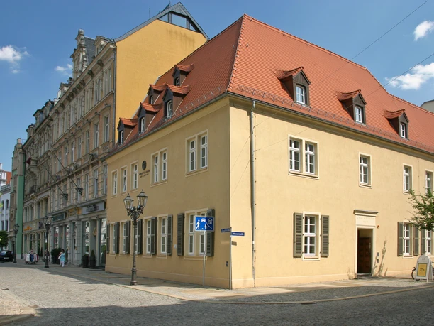008 - Robert Schumann Haus - © Kultour Z.jpg Das Robert Schumann Haus in Zwickau mit gelber Fassade und rotem Dach an einer gepflasterten Straße.
