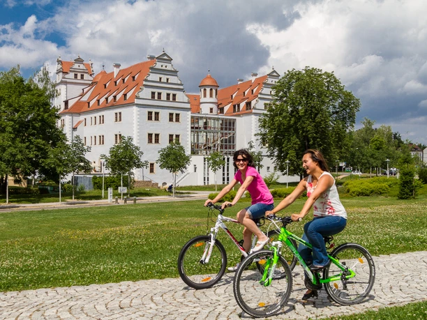 022 - Zwickau - Muldeparadies, Schloss Osterstein - © Kultour Z.jpg Zwei Personen radeln vor dem Schloss Osterstein in Zwickau entlang eines gepflasterten Weges.