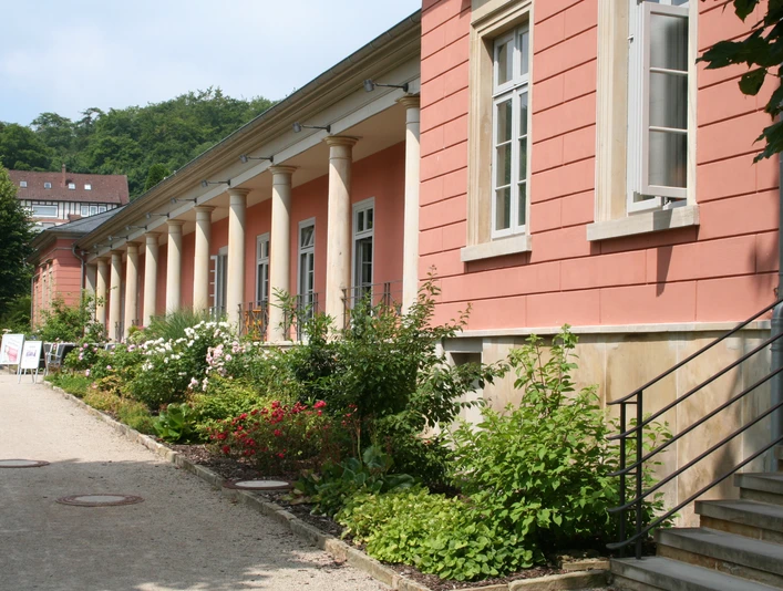 Romantik Bad Rehburg Historisches Gebäude mit roten Wänden und Säulen, flankiert von einem gepflegten Blumenbeet.Historic building with red walls and columns, flanked by a well-tended flower bed.Historisk bygning med røde mure og søjler, flankeret af et velplejet blomsterbed.Historisch gebouw met rode muren en zuilen, geflankeerd door een goed onderhouden bloembed.
