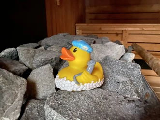 qietscheente Eine quietschgelbe Badeente mit hellblauer Mütze und kleinem Handtuch sitzt auf grauen Steinen.