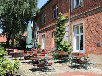 Terrasse mit roten Backsteinen und grüner Bepflanzung, bestuhlt mit Tischen und Stühlen unter freiem Himmel.