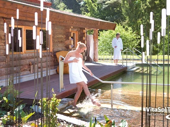 Sauna Naturbadeteich VitaSol Therme Eine Frau und ein Mann in weißen Bademänteln an einem hölzernen Saunahaus mit Naturbadeteich.