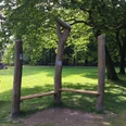 Hörstation am Hermannsdenkmal Holzbank in einer grünen Parklandschaft, umgeben von Bäumen, lädt zur Rast und zum Lauschen ein.