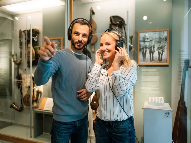 Two people with headphones smile in front of a historical exhibit in the Sorbian Museum.