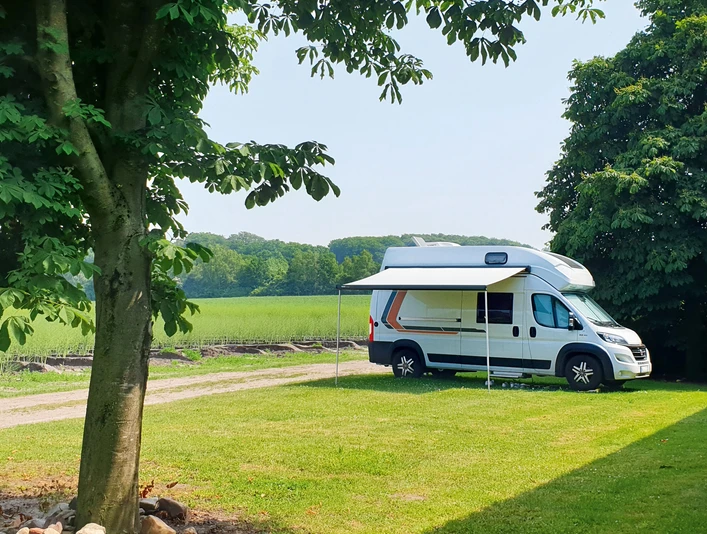 Wohnmobilstellplatz Lüttsche-Hoff Wohnmobil auf grünem Platz am Feldrand, umgeben von Bäumen und ländlicher Natur.