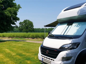 Wohnmobilstellplatz Lüttsche-Hoff Ein Wohnmobil steht auf einem grünen Rasen neben einem Baum, umgeben von Feldern unter klarem Himmel.