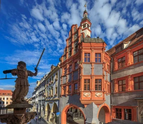 Renaissance building with decorated gable under a blue sky, statue with sword on the left.
