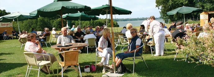 Frucht Café bei Lödings Bauernhof Menschen sitzen an Tischen auf Wiese mit Schirmen