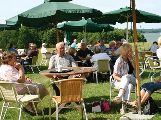 Frucht Café bei Lödings Bauernhof Menschen sitzen an Tischen auf Wiese mit Schirmen