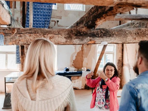 Fachwerk erleben Eine Frau führt zwei Personen durch ein historisches Fachwerkhaus mit freigelegten Holzbalken.
