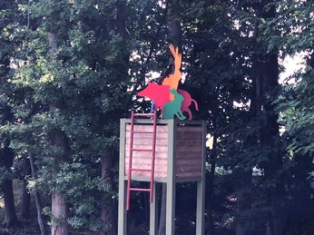 Hochsitz Ein Hochsitz flankiert von Bäumen mit kunterbunten Tierfiguren auf der Balustrade in einem Wald.