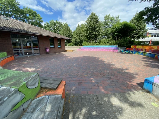 image00011.jpeg Farbenfroh gestalteter Rundplatz aus roten Pflastersteinen, umgeben von bemalten Sitzstufen.