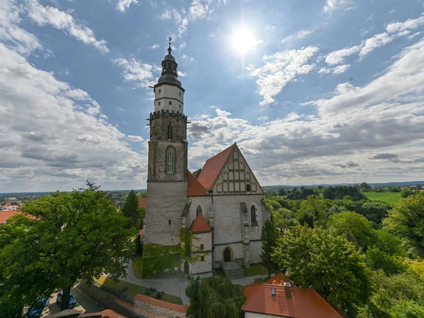 The main church of St. Marien with its striking tower and half-timbered structure, surrounded by trees and a blue sky.
