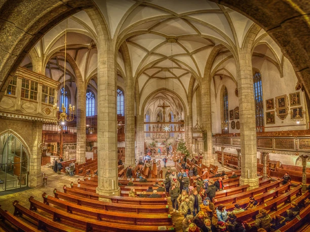 Interior view of St. Mary's Church with ornate vaults and visitors sitting on rows of wooden benches.