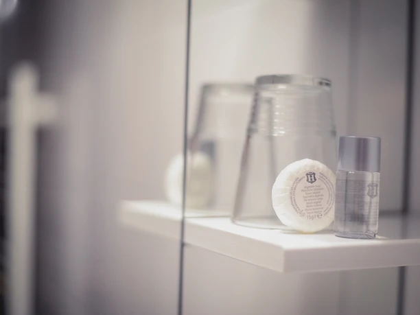 Bierenbacher Hof Ein Badezimmerregal mit zwei Gläsern, einem runden Seifenstück und einer kleinen Shampoo-Flasche.