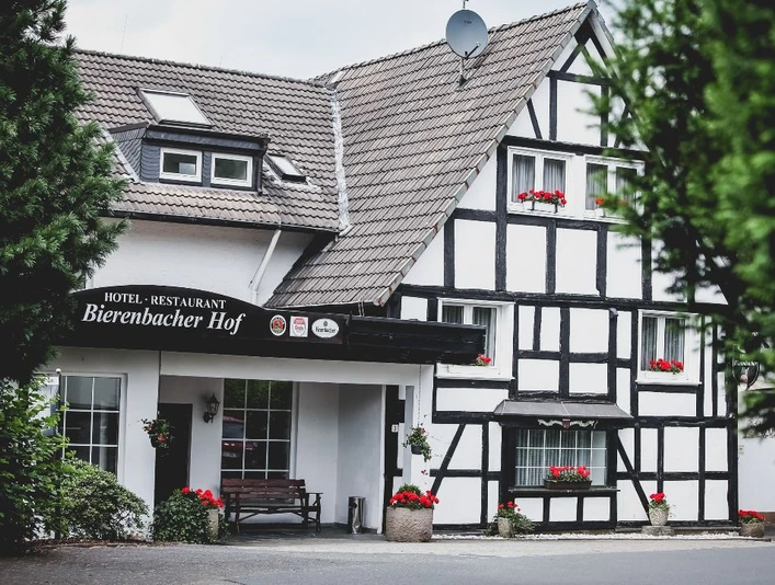 Bierenbacher Hof Ein Fachwerkhaus mit dunklem Holz, weißen Wänden und bunter Blumendekoration im Eingangsbereich.