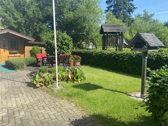 Fewo Hippel_Garten Ein gepflegter Garten mit Rasen, Sonnenschirm, Sitzgruppe, Kinderschaukel und Vogelhaus bei Sonnenschein.
