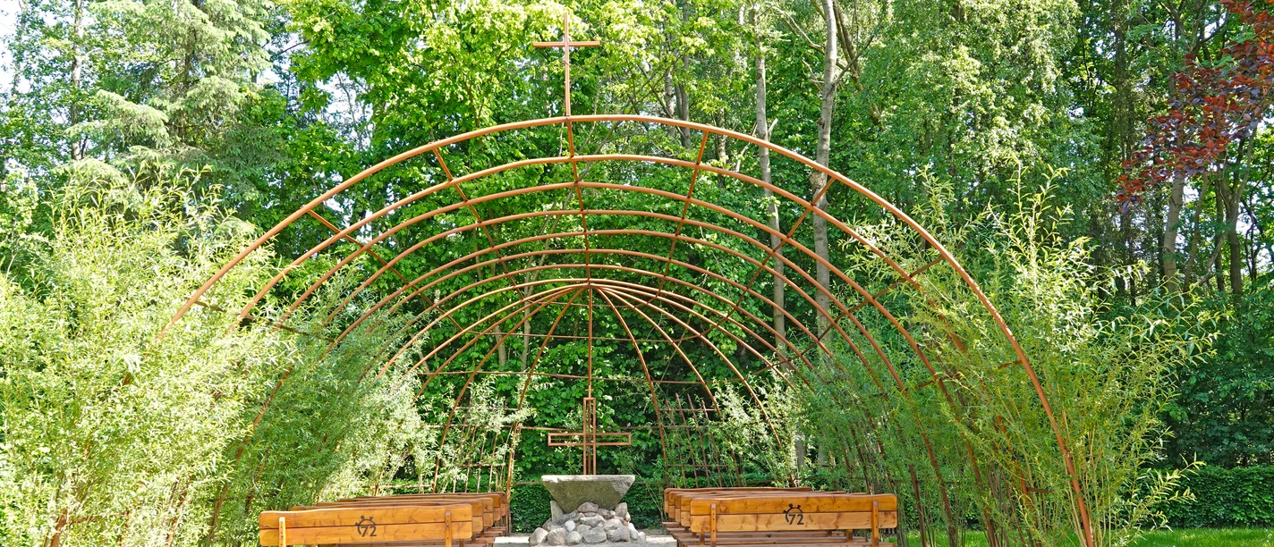 Weidenkirche Bruneforth ©Emsland Tourismus Offene Weidenkirche mit grünem Laubdach, Holzbänken und Altar aus Stein inmitten hoher Bäume.