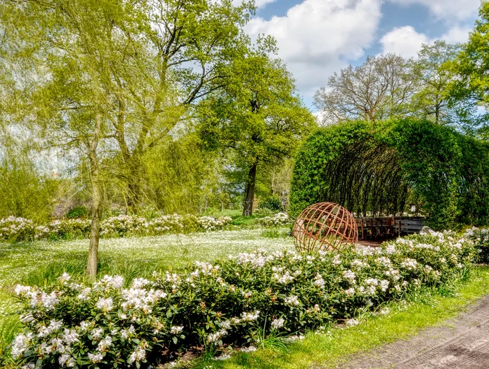 Weidenkirche Börger ©Naturpark Hümmling Grüne Weidenkirche aus verflochtenen Zweigen, umgeben von blühenden Sträuchern und alten Bäumen.