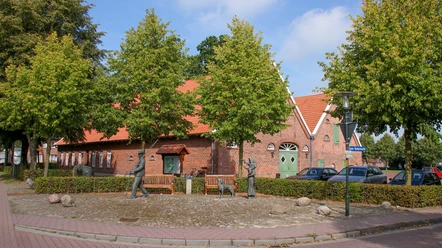 Krull's Hus Backsteingebäude mit rotem Ziegeldach, grünen Türen und Figuren auf einem gepflasterten Platz davor.