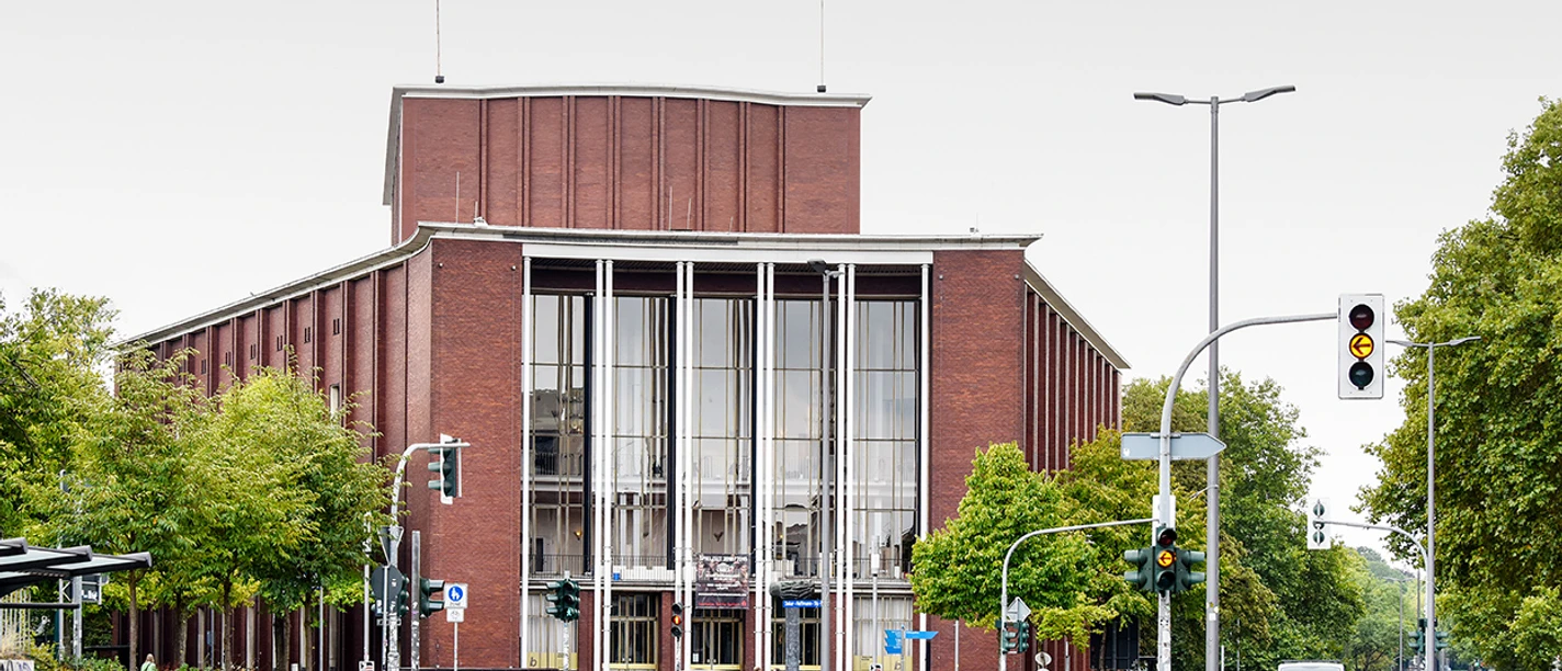 Schauspielhaus Bochum <p>Das Bild zeigt ein modernes Gebäude mit großer Glasfassade an einer belebten Straßenkreuzung.</p>